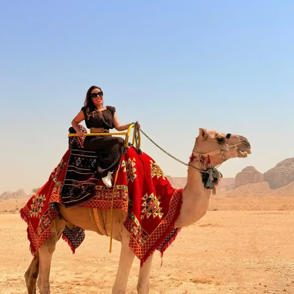 A traveler enjoying a traditional camel ride across golden sand dunes, showing the Reasons Why Camel Ride Riyadh Is a Must-Do for desert explorers.