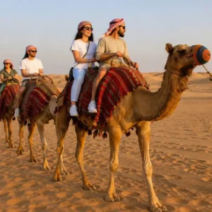 "How safe is an evening desert safari – tourists enjoying a camel ride across golden sand dunes at sunset with guides ensuring safety"